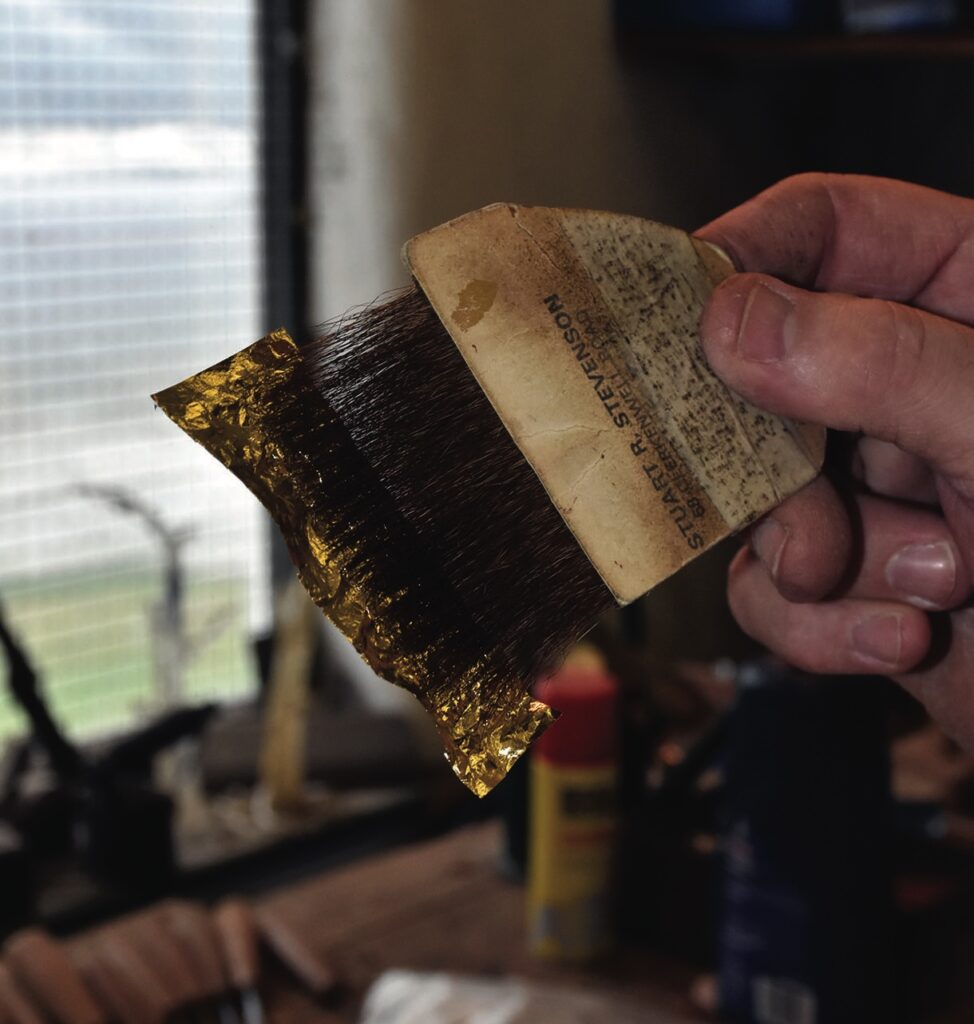 A hand holding a worn paintbrush in workshop.