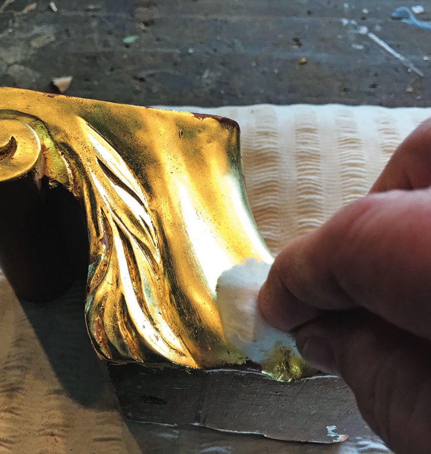 Restoring gilt wood furniture corner with cloth.
