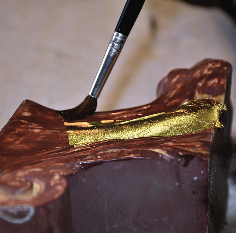 Applying gold leaf to ornament with brush