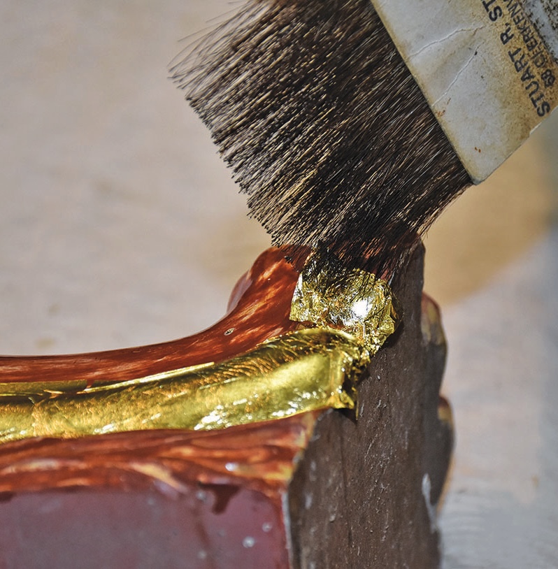 Brush applying gold leaf to wooden frame