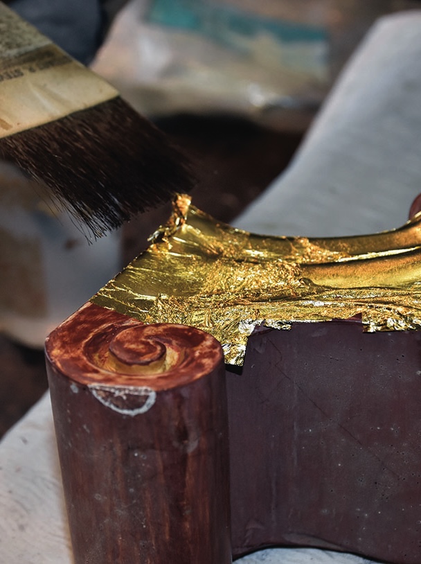 Applying gold leaf with brush on wood frame.