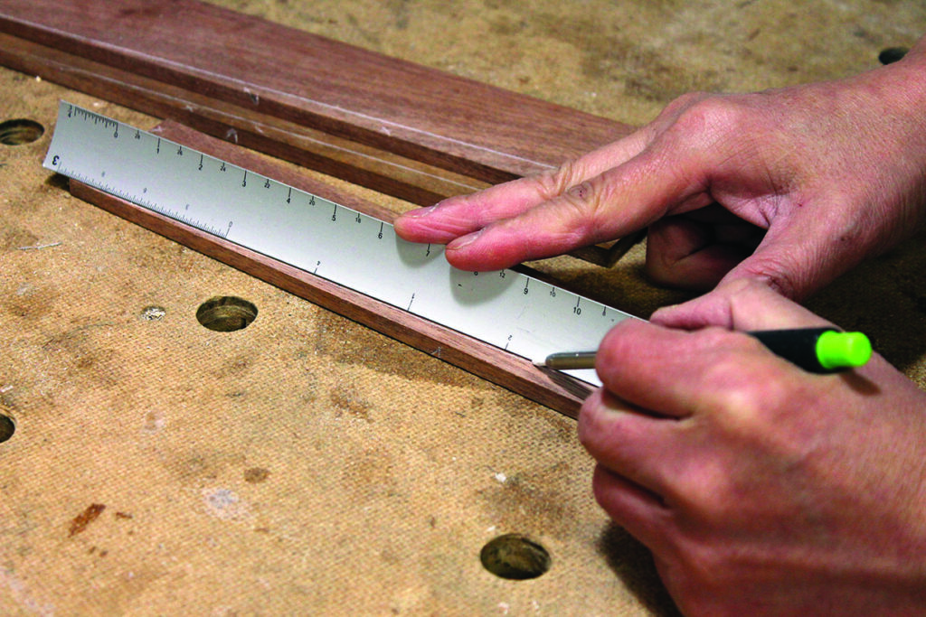 Carpenter marking wood with ruler and pencil.