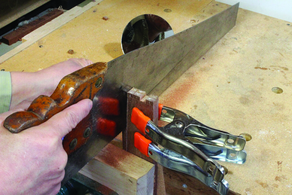 Carpenter sawing wood with hand saw and clamps.