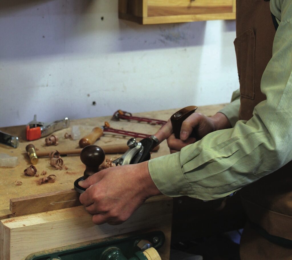 Person using hand plane in woodworking workshop.
