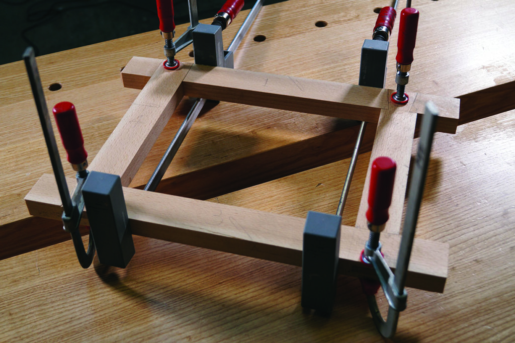 Wooden frame clamped on workbench with red handles.