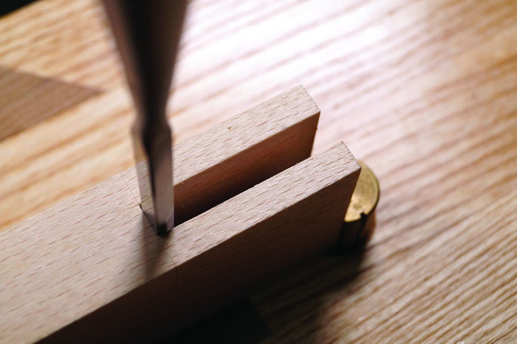 Woodworking chisel cutting dovetail joint in wood.