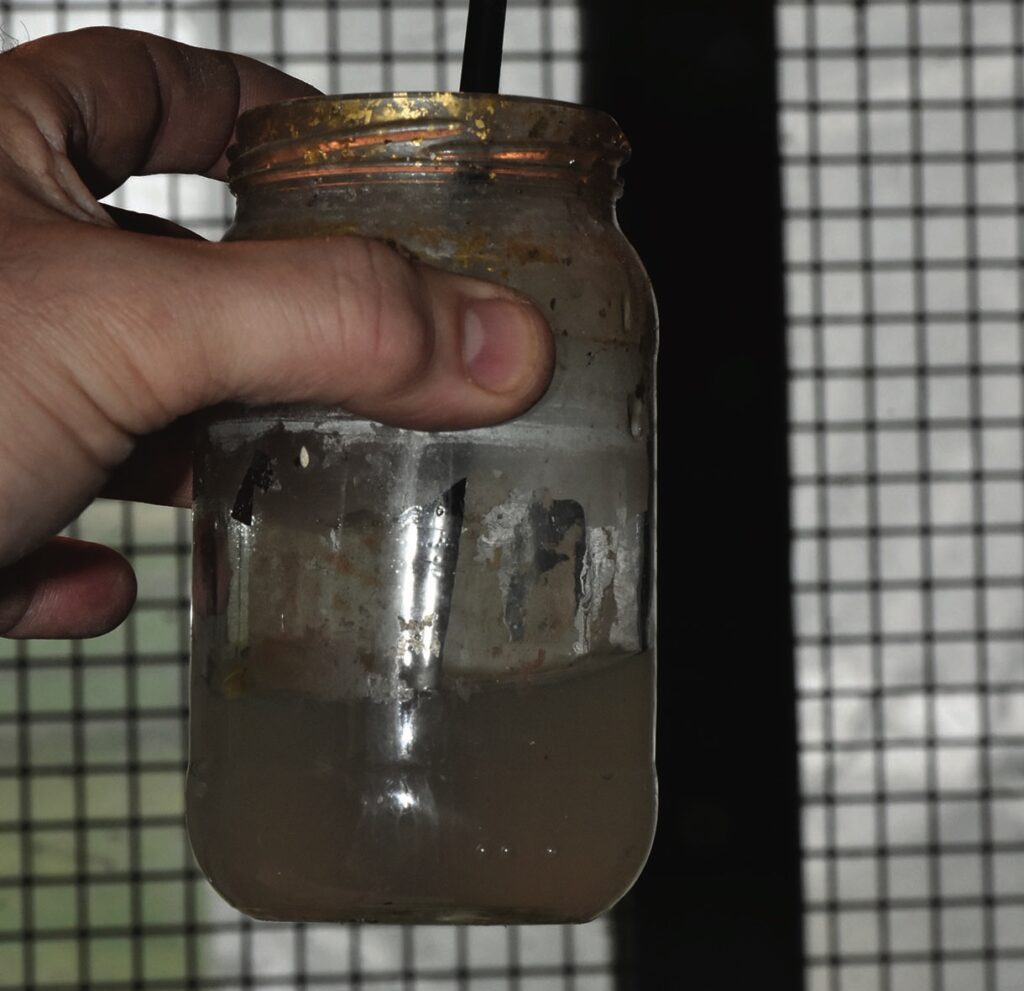 Hand holding dirty jar with liquid and straw.