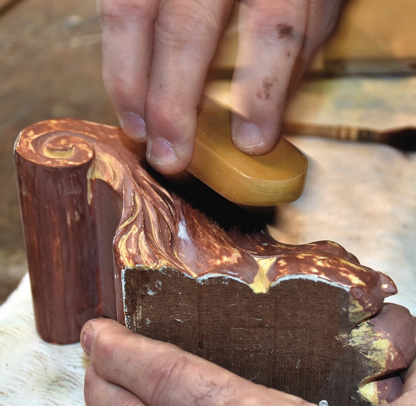 Hand applying gold leaf to wooden ornament.