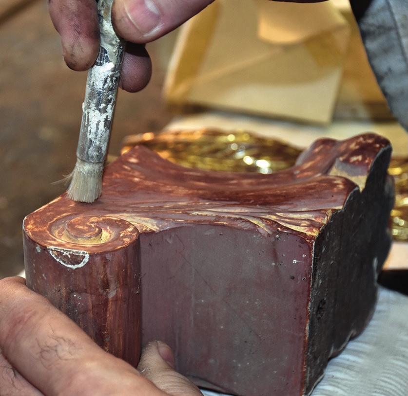Artist gilding a wooden sculpture with a brush.