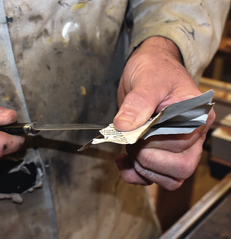 Person testing knife sharpness on paper strip.