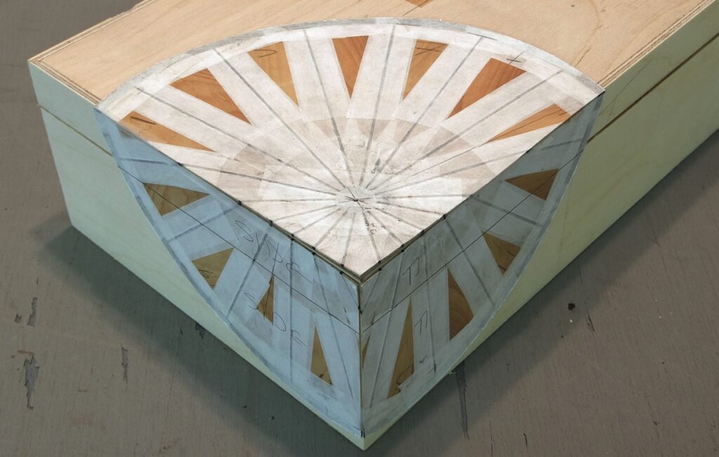 Wooden corner model with radial design pattern.