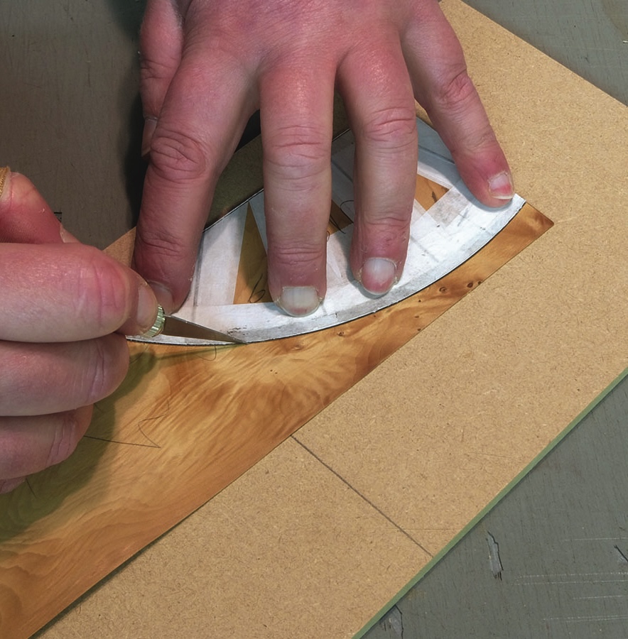 Craftsman cutting intricate wood veneer design by hand.