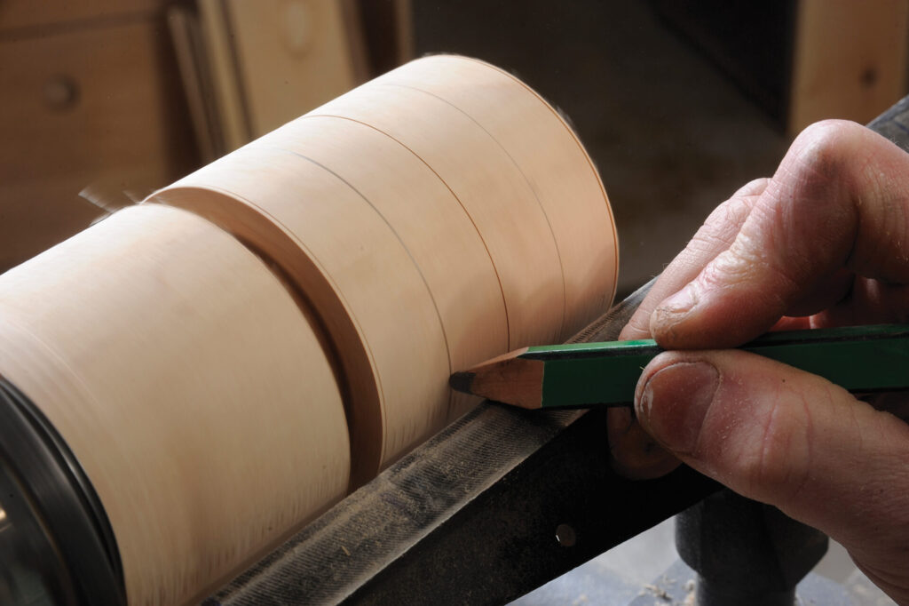 Craftsman marking spinning wood with pencil.