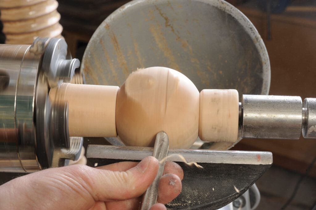 Wood lathe shaping a wooden sphere.