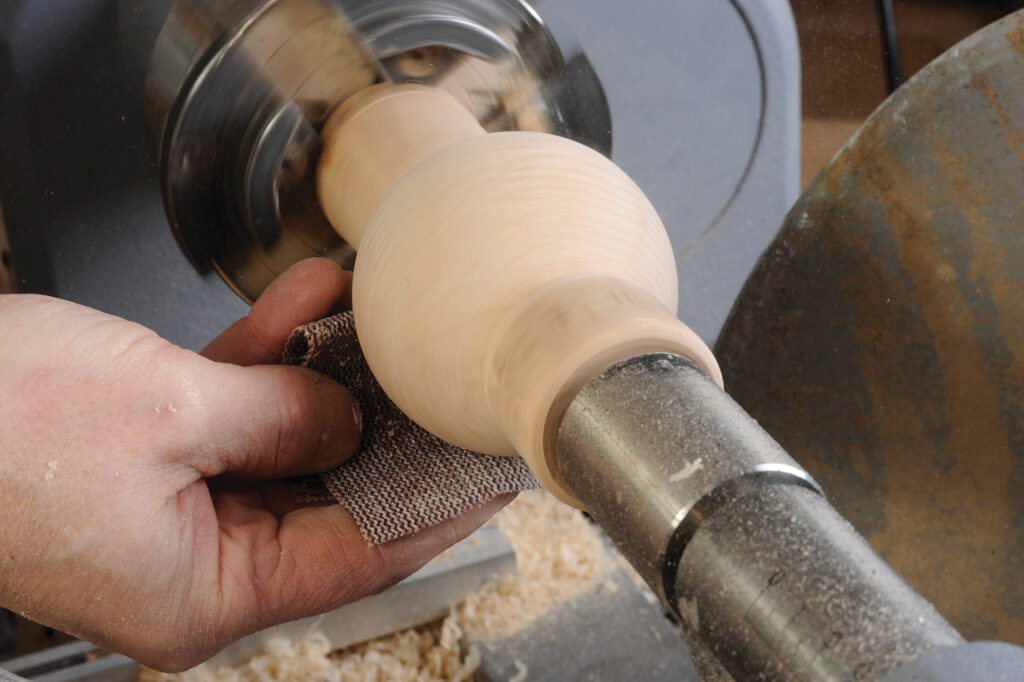 Person sanding wood on a lathe machine.
