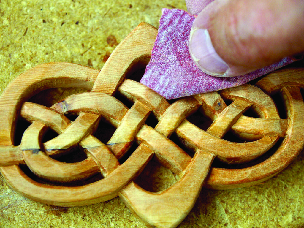 Sanding wooden Celtic knot carving detail.