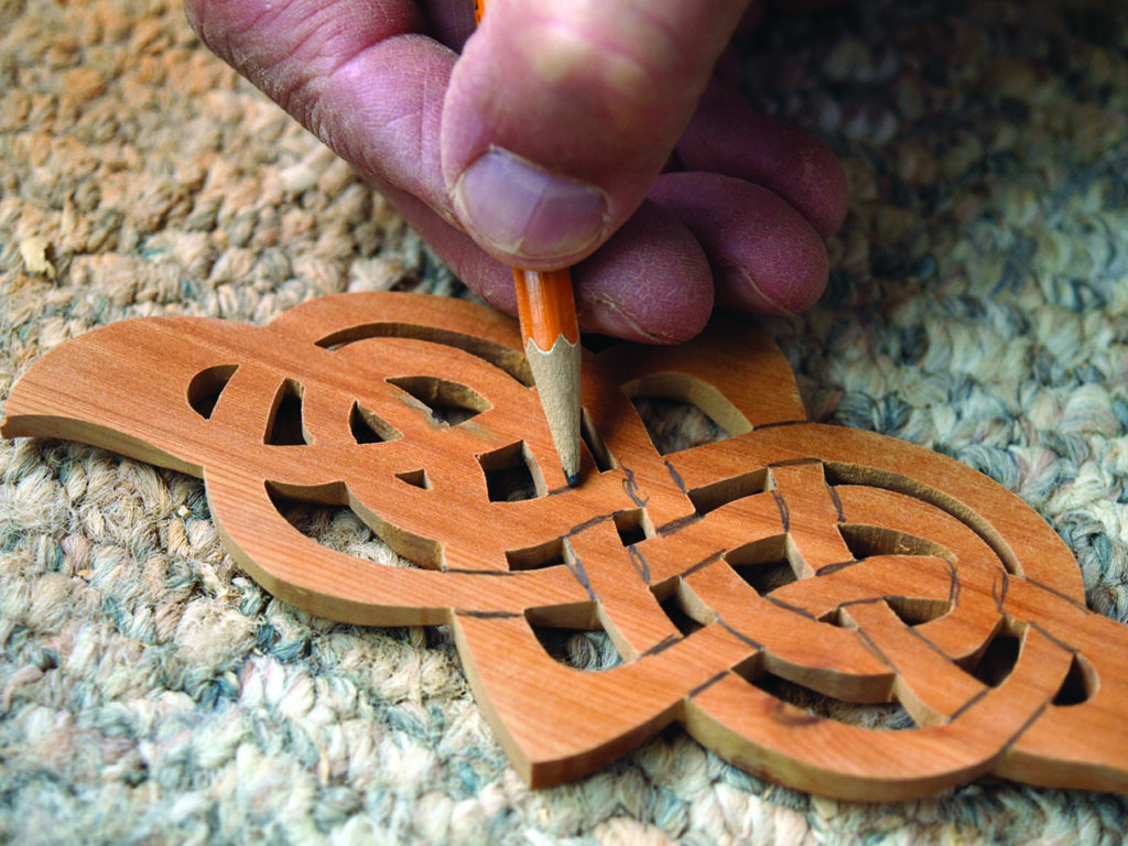 Hand crafting intricate wooden design with pencil.