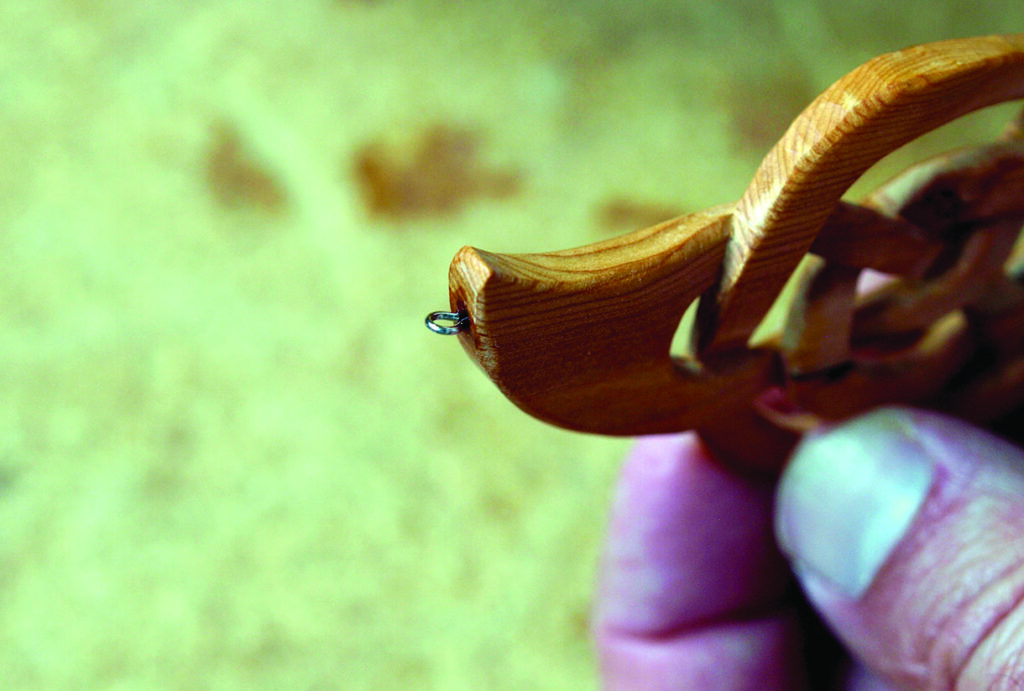Hand holding intricate wooden sculpture detail.