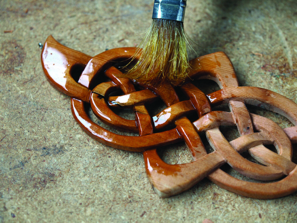Applying finish to wooden Celtic knot carving.