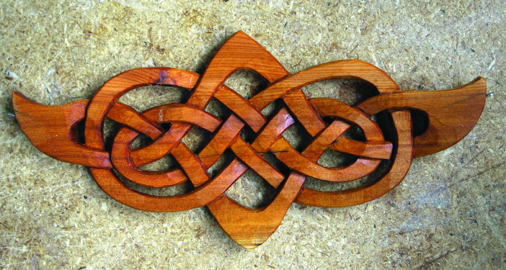 Intricate wooden Celtic knot carving on wood background.