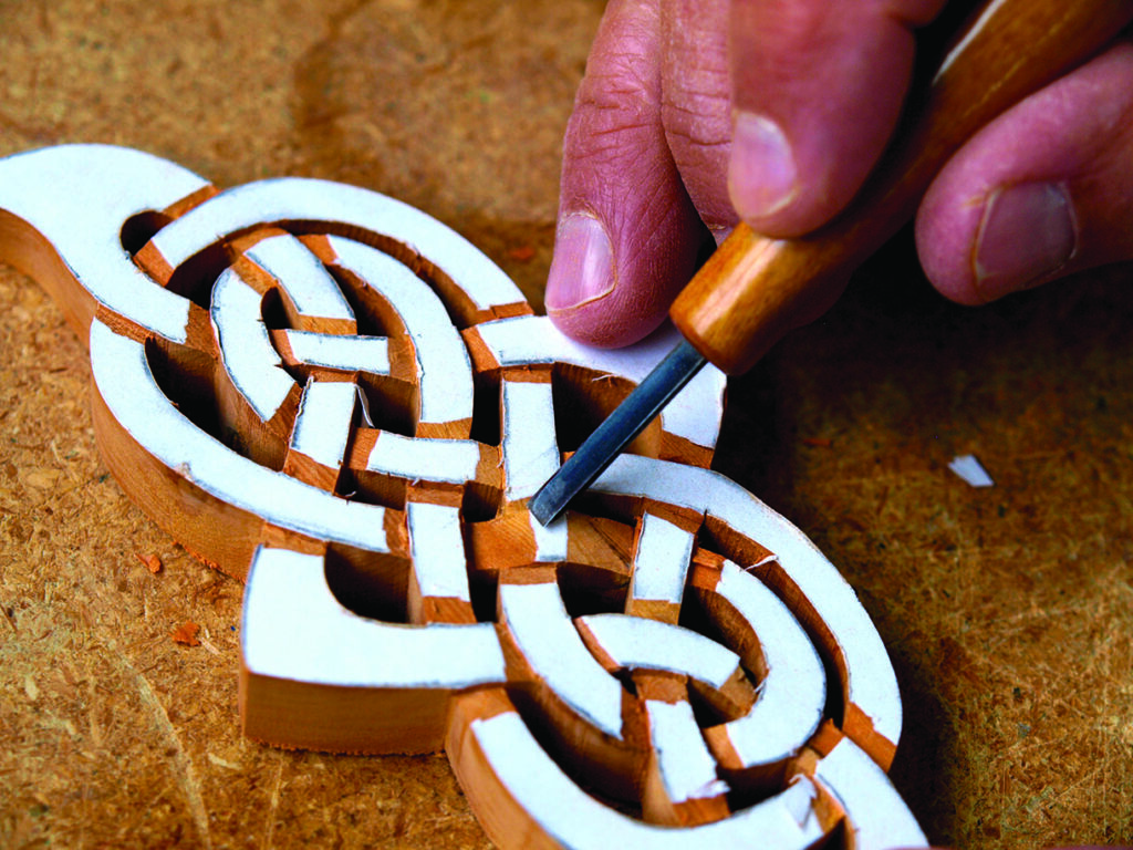 Hand carving detailed wood design with chisel.