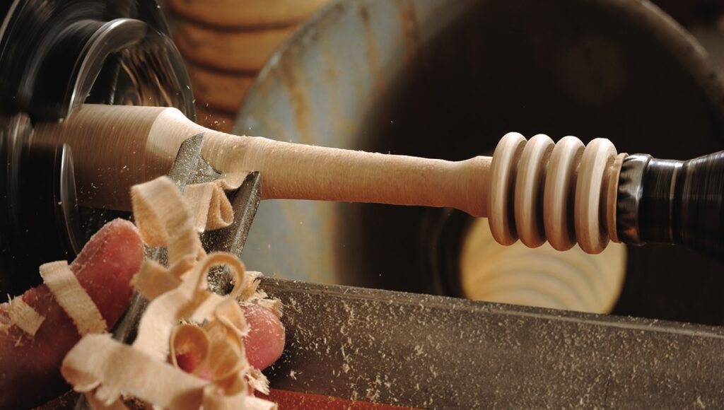 Woodturning on lathe with shavings falling off.