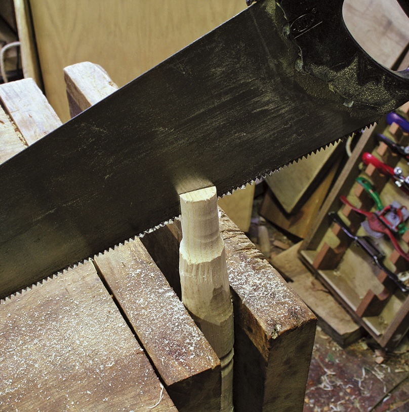 Hand saw cutting wooden dowel in workshop.