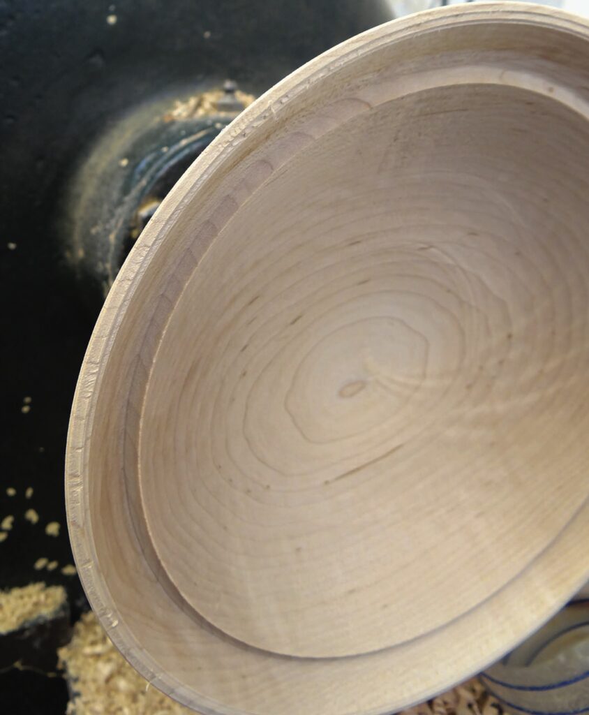 Wooden bowl on a pottery wheel with shavings.