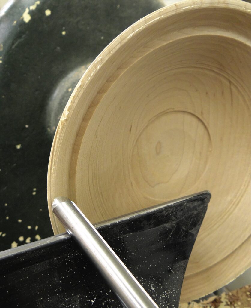 Woodturning lathe carving wooden bowl in progress.