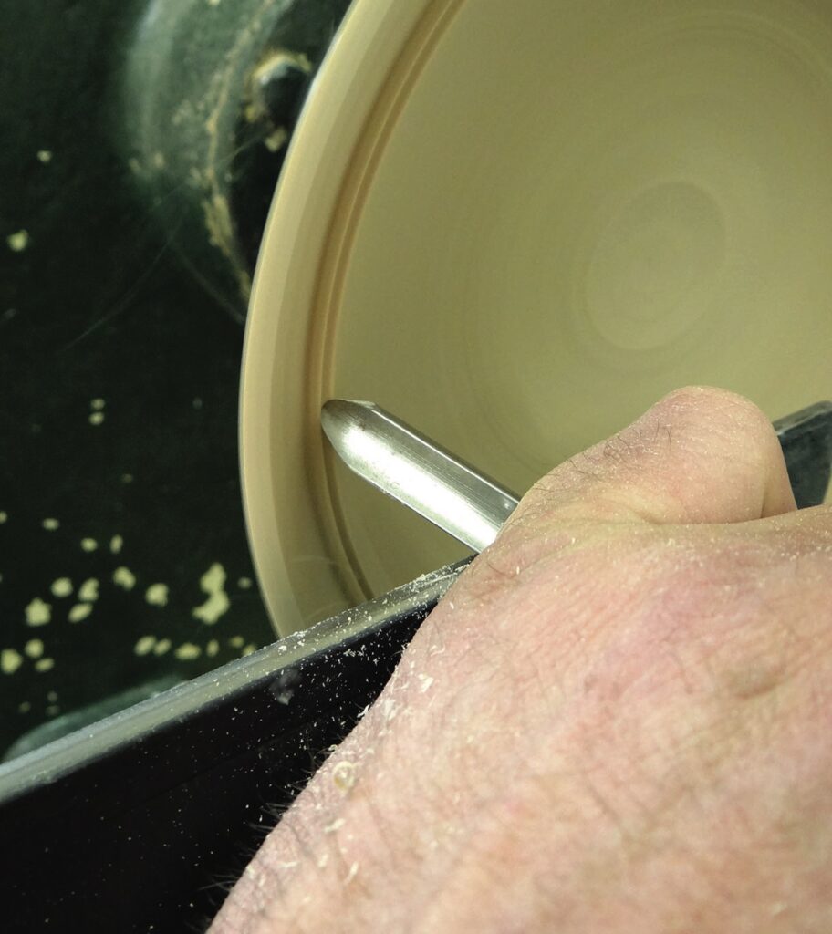 Person woodturning on lathe with chiseling tool.