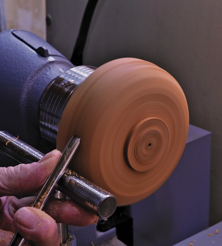 Woodturning on lathe with hand tool.