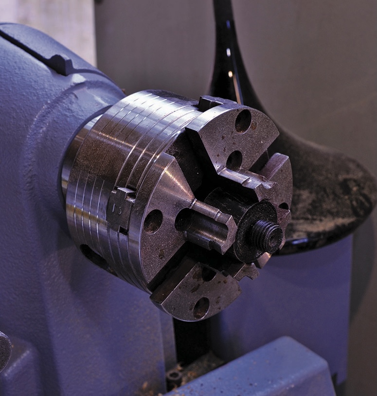 Metal lathe chuck in a workshop setting.