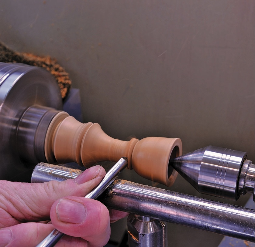 Woodturning on lathe with hands and chisel.