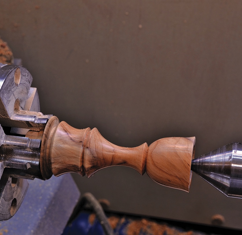 Wood lathe turning intricate wooden piece.