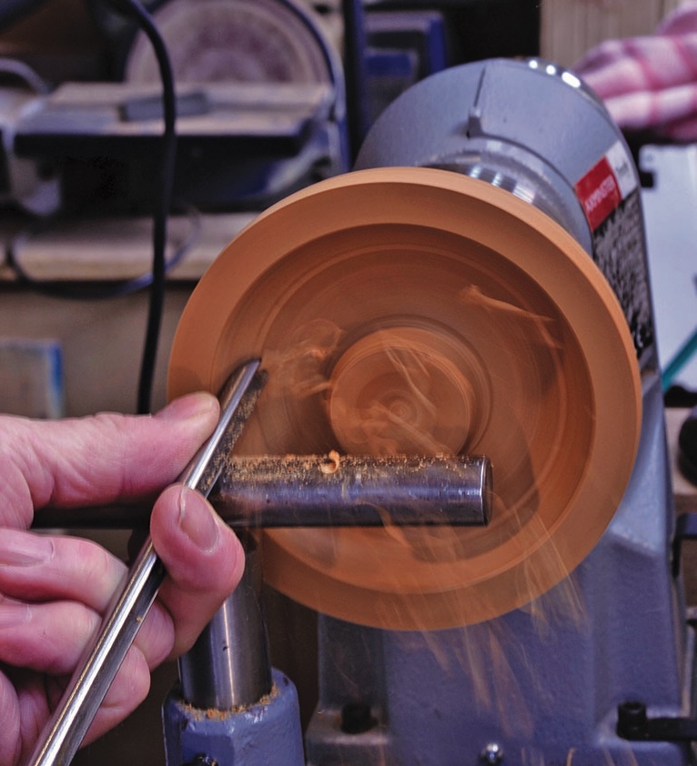 Person shaping wood using lathe in workshop.