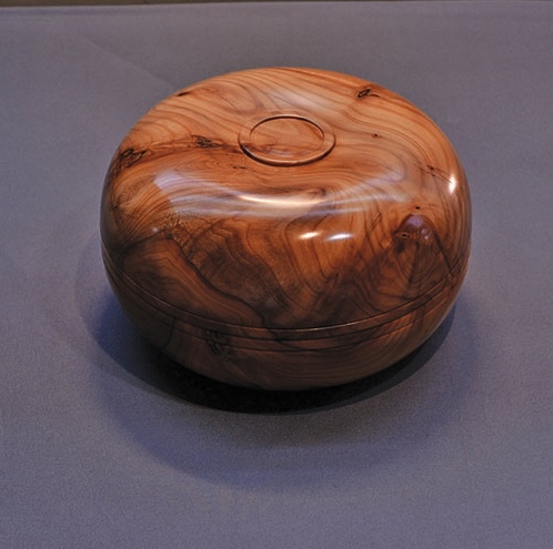 Round wooden box with polished finish on table.