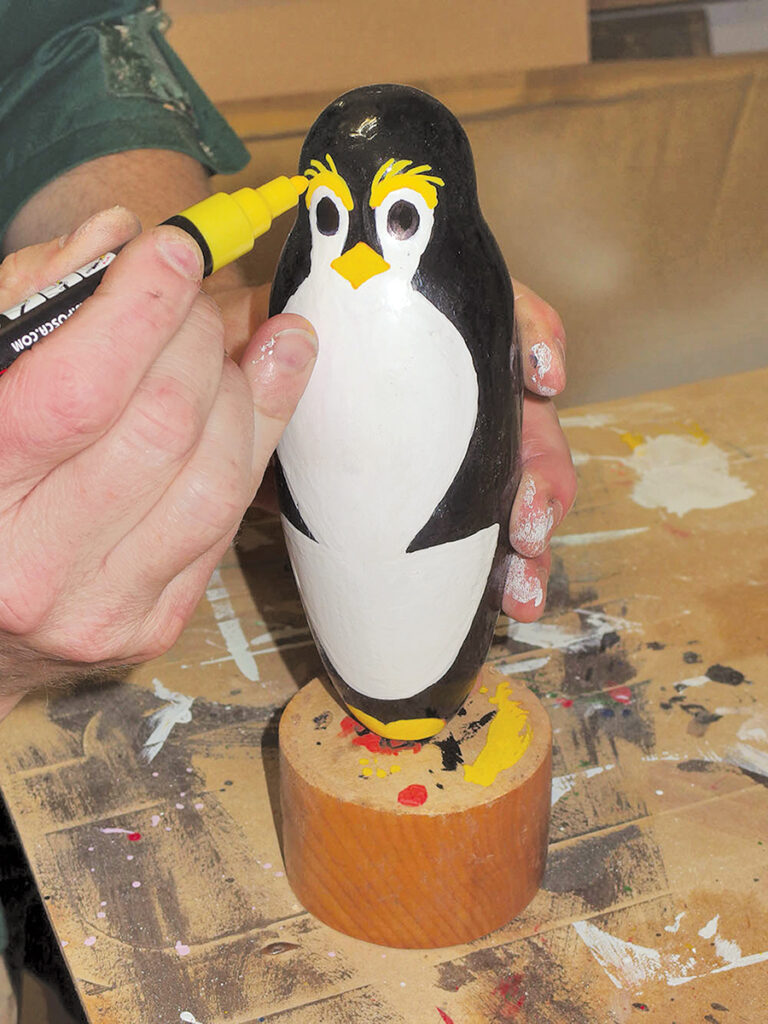 Person painting wooden penguin with yellow marker