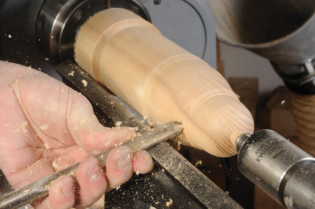 Woodturning process with hand and tool on lathe.