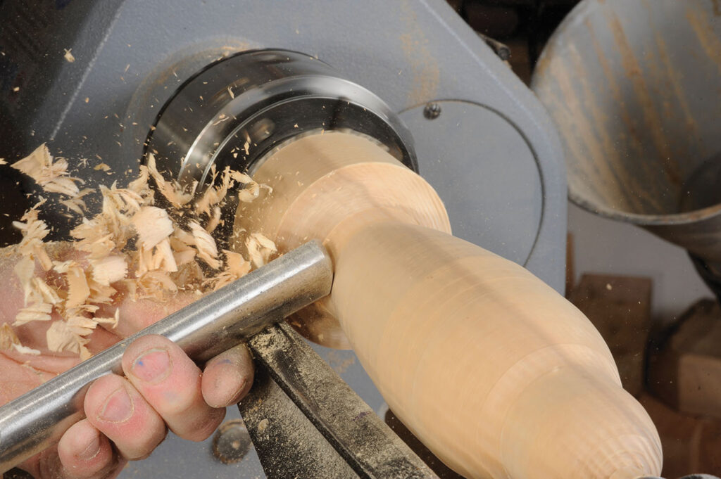 Woodturning on lathe with wood shavings flying.
