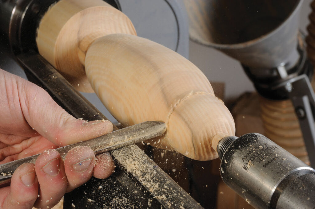 Person woodturning on lathe with chisel tool.