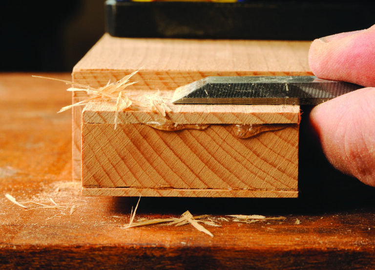 Chisel smooths wood block with curling shavings.