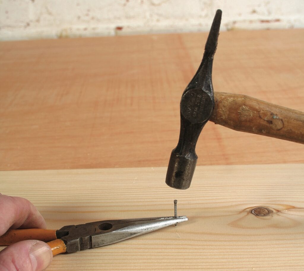 Hammer and pliers holding nail on wood.