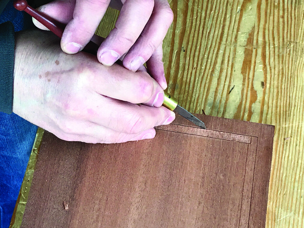 Person carving precise groove into wood veneer.