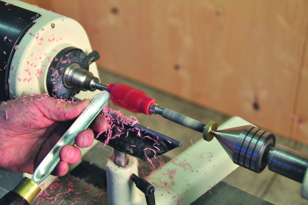 Woodturning a pink acrylic pen on lathe machine.
