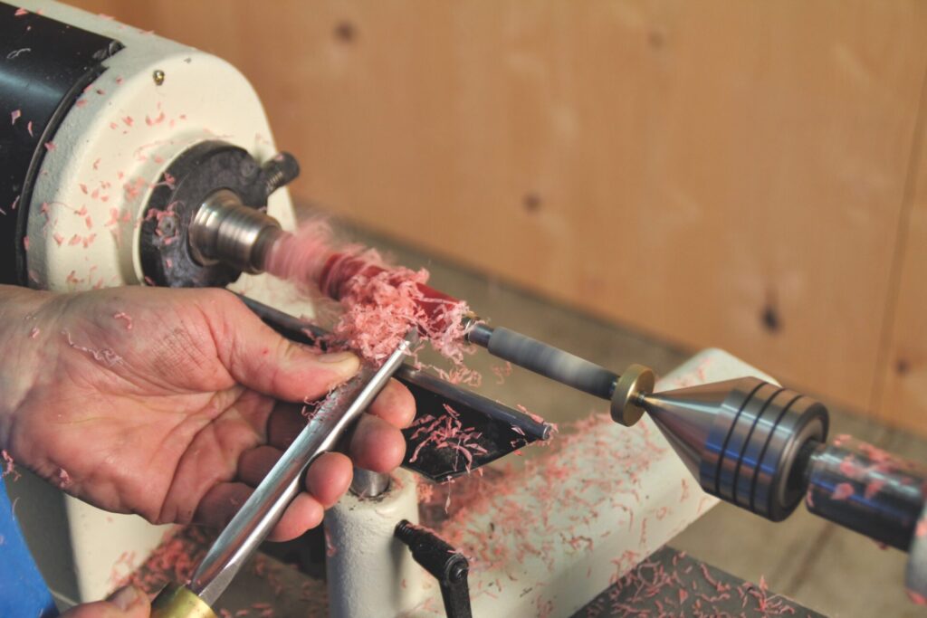 Lathe woodturning with hand tool and shavings.