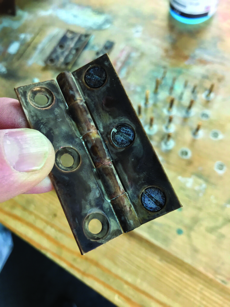 Person holding old brass hinge on wooden table.