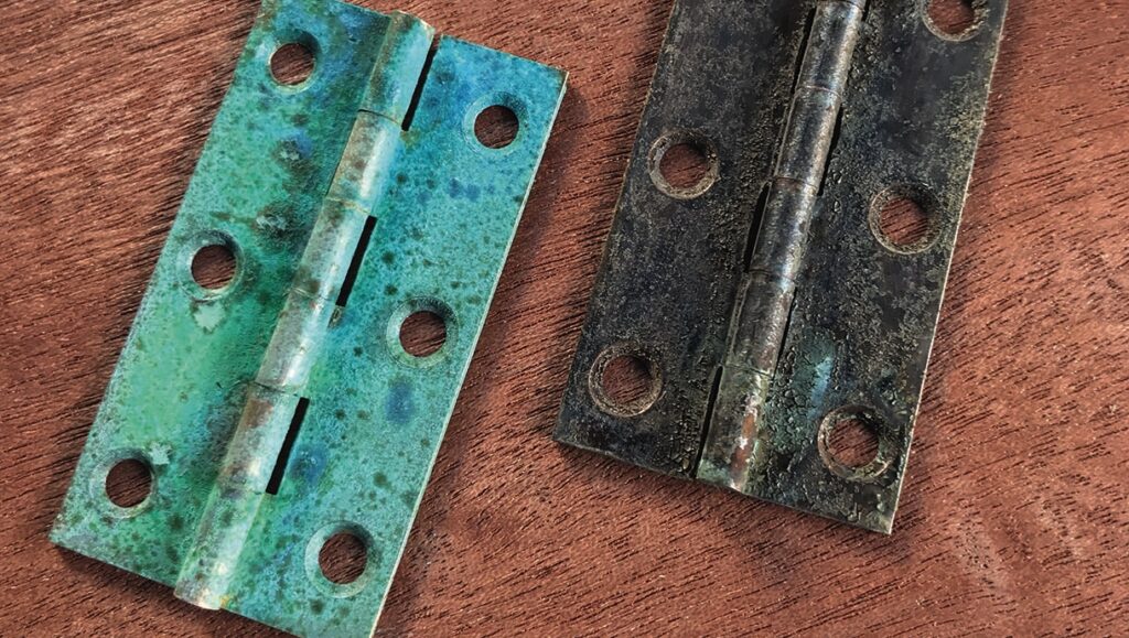 Two rusty door hinges on wooden surface.