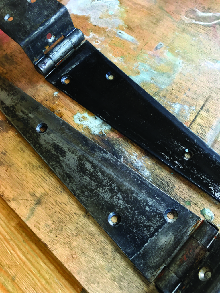 Two old metal hinges on a wooden surface.