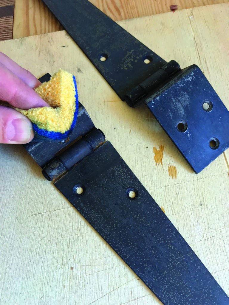 Cleaning metal hinges with sponge on wood surface.