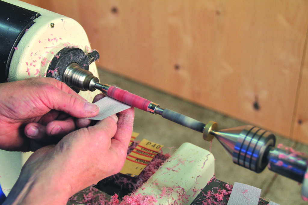 Person sanding on a lathe machine in workshop.